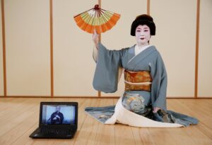 A geisha sits, holding a fan upside down.