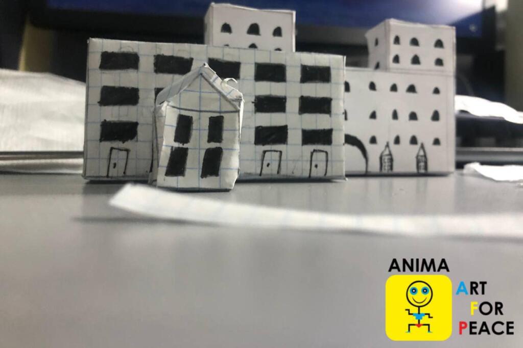 This is an image of a paper white house with ANIMA Art for Peace sign. This is an image of a house made by a student from ANIMA Art for Peace and his 10-year old brother - Бальков Вадим та Антон/ Wadym and Anton Balkowy – before they escaped Kharkiv/Ха́рків.