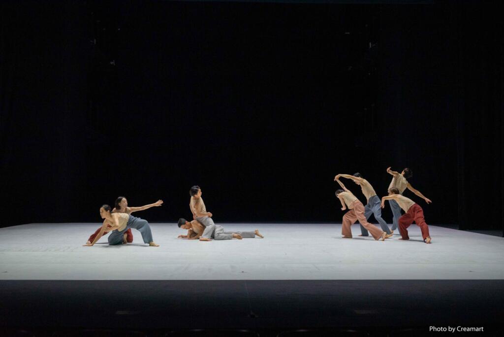 A group of dancers are performing different gestures on a bare stage at the same time.